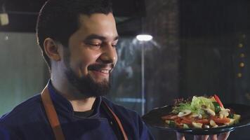 Handsome male chef smiling while holding a vibrant plate of fresh salad video