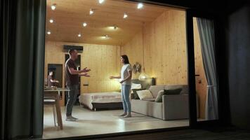 Young couple having a heated discussion in their modern, minimalist style apartment, observed from outside through a large window, highlighting the tension and emotional distance between them video