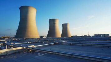 Wide-angle view of industrial cooling towers at a power plant facility under a clear blue sky, surrounded by pipelines and infrastructure, symbolizing energy production and large-scale video