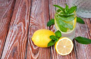 Natural lemonade with lemon and fresh mint in a glass on wooden table. Refreshing summer drink. Copy space. photo