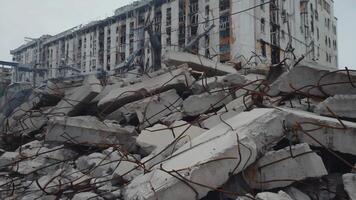 colapsado hormigón estructura con retorcido varilla en frente de un dañado edificio, demostración destrucción, escombros, y estructural fracaso a menudo visto después demolición, desastre, o urbano decaer video