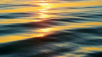 Golden sunlight reflecting on gentle ocean waves during sunset creating a peaceful and abstract water surface perfect for backgrounds, nature textures, relaxation themes, and sea view video