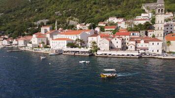 Aerial view of a boat sailing in the Adriatic Sea near the coast with the background of the tourist town of Perast, Montenegro video