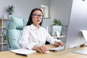 Portrait of Asian business woman with call headset, consultant and tech support, working in modern office, looking confidently at camera. photo