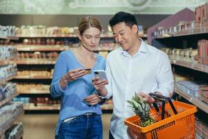 Diverse family couple Asian man and woman in supermarket satisfied and happy shopping, using app on phone to select products and shopping list, use credit card. photo