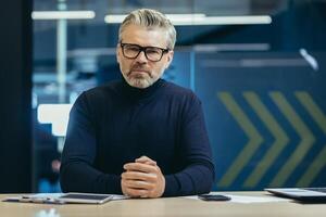 Portrait of an older gray-haired man in glasses of a teacher, trainer, coach who sits seriously in front of the camera and communicates, teaches on a call. photo