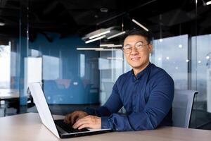 Successful asian businessman smiling and looking at camera, programmer porter inside office using laptop writing code for software security. photo