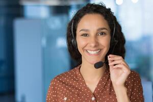 Close up photo portrait of young beautiful hispanic woman, business woman smiling and looking at camera, receptionist using headset for call, happy and successful call center worker