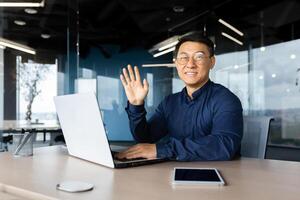 Portrait of a young handsome Asian male programmer working in the office at a laptop. Confidently smiling and looking at the camera. photo