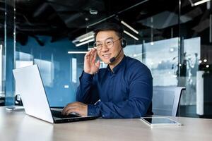 Cheerful and smiling office worker with call headset, Asian customer support tech of online store, smiling and talking consulting. the man works inside the office. photo