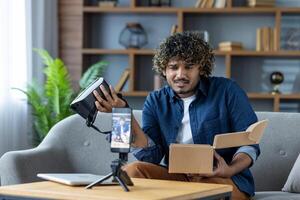 Man writes negative review about product purchased in online store. Influencer blogger sits at home on sofa in living room, uses tripod and phone to record online stream photo