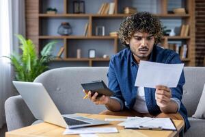 Man concerned about high utility bills while using laptop and calculator photo