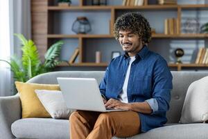 Smiling man using a laptop while sitting on a comfortable couch at home photo
