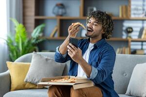 Man enjoying pizza while taking a selfie on the couch with smartphone photo