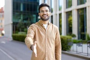 Smiling man extending hand for handshake outside modern building photo