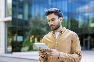 Young man using digital tablet outside modern office building, focusing on business tasks photo