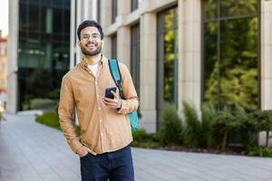 Smiling young student holding smartphone outdoors on a university campus photo