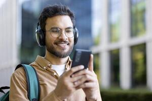Smiling man using smartphone with headphones outdoors enjoying music and technology on a bright day photo