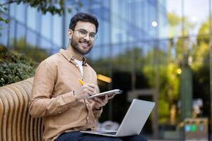Smiling young man working with laptop and tablet in outdoor setting showcasing productivity and technology photo
