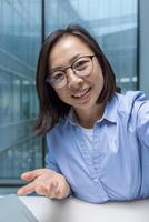 Young businesswoman using phone app for call, smartphone camera view. Office worker looking at camera smiling and talking to colleagues and partners sitting at desk inside office. photo