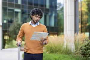 Businessman holding map outside office building looking confident and focused. Man standing with suitcase handle, prepared for travel. Professional planning journey, showcasing navigation skills photo