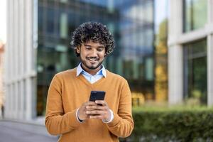 Young professional smiling while using smartphone in urban setting. Dressed in casual attire, enjoying communication and connectivity during outdoor break near office buildings. photo