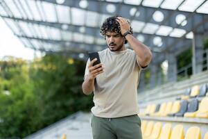 Sad disappointed man with phone in hands walking in park, athlete after fitness and active physical exercise, uses app to track workout progress. photo