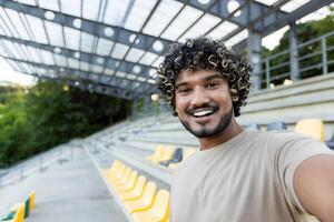 Young man smiling and taking a selfie on stadium bleachers before or after a workout or game. photo