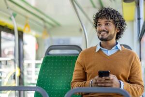 Happy man with phone in hands rides in public transport, passenger smiles and looks out the window, uses smartphone app to browse social media. photo