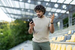 Dissatisfied athlete checking app on phone, man with smartphone in hands dissatisfied with achievement results and training exercises. photo