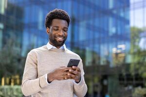Young successful businessman walking through the city with a phone in his hands, the man is typing a text message and browsing online social networks. Company employee at lunchtime. photo