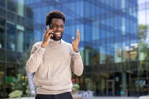 An african-american businessman looks stressed while having a phone call outdoors, in front of a modern building. He is visibly angry. photo