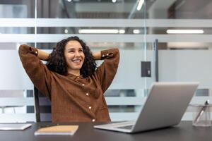 Successful businesswoman well done, successfully completed current project. Office worker with hands behind head resting and relaxing, enjoying results of achievement. photo