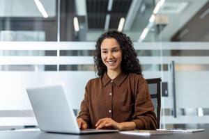 Successful joyful businesswoman working with laptop inside office. Company employee typing on keyboard, smiling happily, satisfied with results of achievement at work. photo