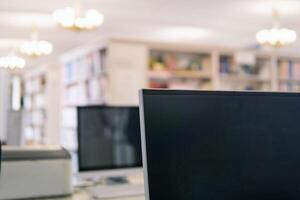 Blurred background of library with computer monitor on a foreground and bookshelfs photo