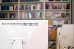 Close-up of a white computer monitor in a library with bookshelf in the background photo