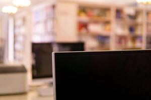 Blurred interior of traditional library with computer monitor on a foreground and bookshelfs photo