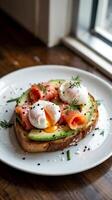 A delicious breakfast dish featuring poached eggs, smoked salmon, and avocado is served on a slice of toasted bread, garnished with black sesame seeds and fresh herbs photo