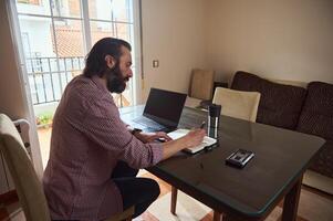 Man Working Remotely at Home Planning Projects with a Notebook and Laptop photo