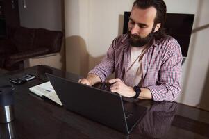 Focused Man Working on Laptop While Taking Notes in a Home Office photo