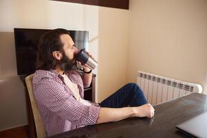 Man Relaxing While Drinking Coffee at Home Desk During Casual Work Hours photo