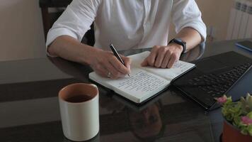 Man Writing Notes in Journal While Working with Laptop in Office photo