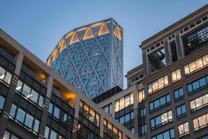 Evening view of 22 Bishopsgate in London with its illuminated diamond patterned facade, surrounded by lit office buildings under a clear sky. photo