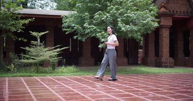 Handheld side view shot, Solo female tourist enjoys taking photos with camera while taking a leisurely stroll amidst serene surroundings and the cultural richness of the place. video