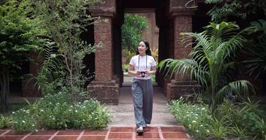 Female tourist enjoys taking photos with camera while taking a leisurely stroll amidst serene surroundings and the cultural richness of the place. video