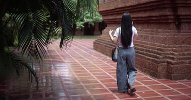 Handheld back view shot, Solo female tourist enjoy talking with her friend on smartphone while taking a leisurely stroll amidst serene surroundings and the cultural richness of the place. video