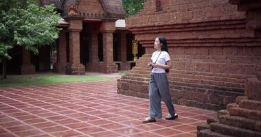 Handheld shot, Asian female tourist enjoys taking photos with camera while taking a leisurely stroll amidst serene surroundings and the cultural richness of the place. video
