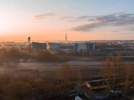 Serene morning scene in Riga, Latvia, featuring the Riga TV Tower in the distance, railway tracks in the foreground, and modern buildings in light mist. photo