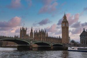 The Palace of Westminster and Elizabeth Tower, with Westminster Bridge over the River Thames, set against a pink and blue evening sky in London. photo