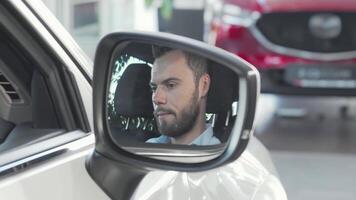 Joyful man proudly displaying car keys in side mirror of his sleek vehicle video